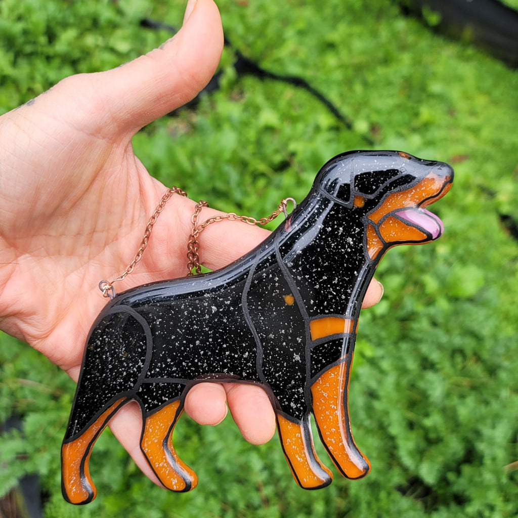Rottweiler Glass Urn Ashes-Infused-Glass Ornament   A hand holding a glass cremation urn suncatcher with a silhouette of a Rottweiler dog with cremation ashes inside. infusion glass artist Joele Williams ashes infused glass