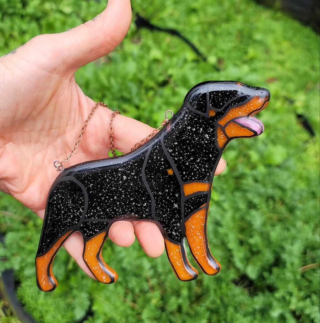 Rottweiler Glass Urn Ashes-Infused-Glass Ornament   A hand holding a glass cremation urn suncatcher with a silhouette of a Rottweiler dog with cremation ashes inside. infusion glass artist Joele Williams ashes infused glass