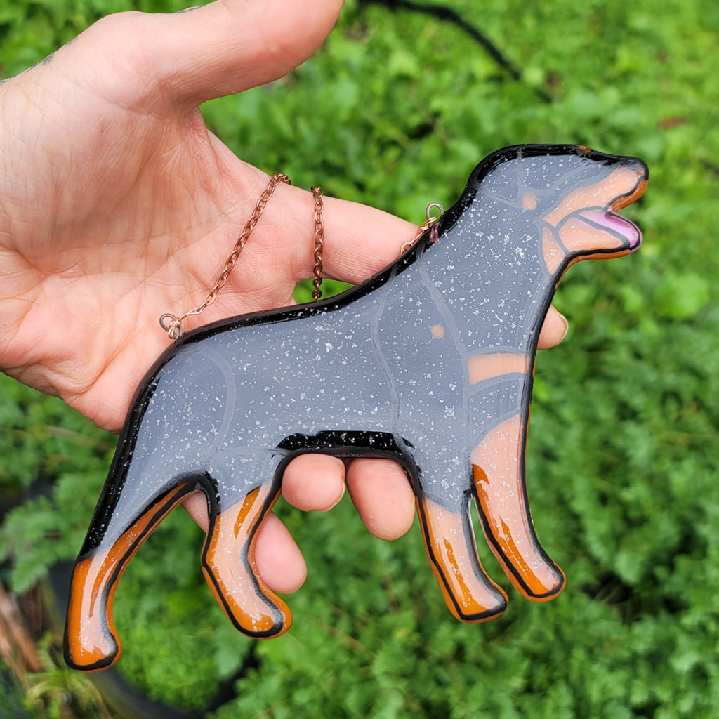 Rottweiler Glass Urn Ashes-Infused-Glass Ornament   A hand holding a glass cremation urn suncatcher with a silhouette of a Rottweiler dog with cremation ashes inside. infusion glass artist Joele Williams ashes infused glass
